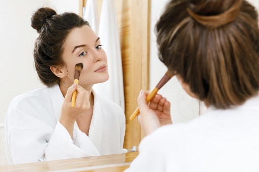 Woman looking in the mirror and applying foundation or blusher on her face